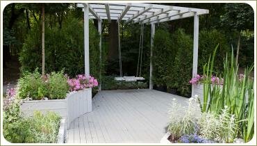 Белая конструкция и качели на фоне цветникоа