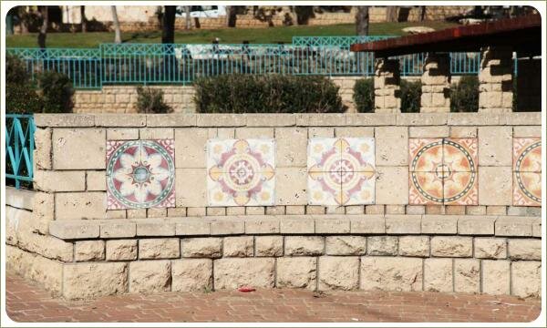 Небольшая стенка из светлого камня с орнаментом и скамья и мощёная площадка из камня