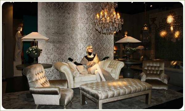 Роскошный бежевый интерьер с велюровым диваном и креслами, обои с коричневым геометричным рисунком, на диване сидит манекен в красивом платье