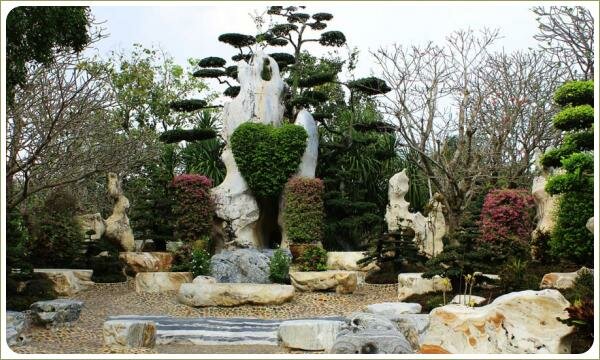 Причудливые формы камней светлого цвета и кустарник в форме сердца на фоне сформированных крон растений