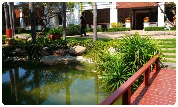 Мостик для пейзажного пруда. Сад в Таиланде Лёгкий мостик на фоне пруда с бетонными берегами и растительностью