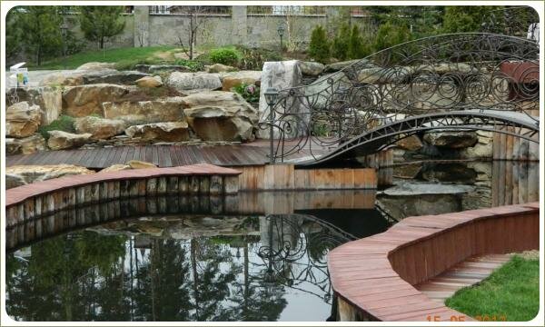 Пруд с берегом из дерева. Урал Деревянные берега у пруда и мостик и каменный каскад и растения