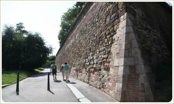 Старинная стена из разного камня со следами разрушения и дорога и лужайка 