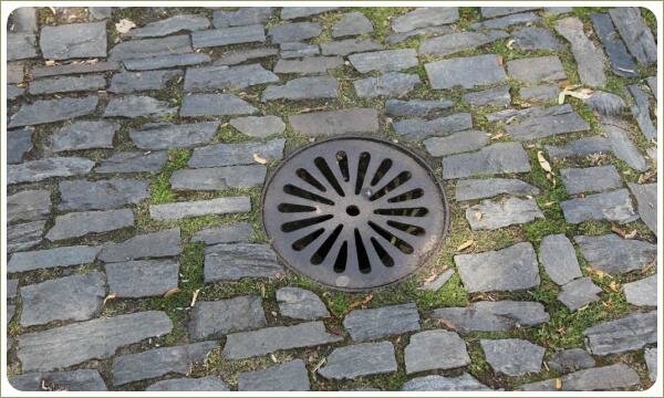 Камень и люк - мощение Праги Серый камень поросший мхом и маленький люк на площадке
