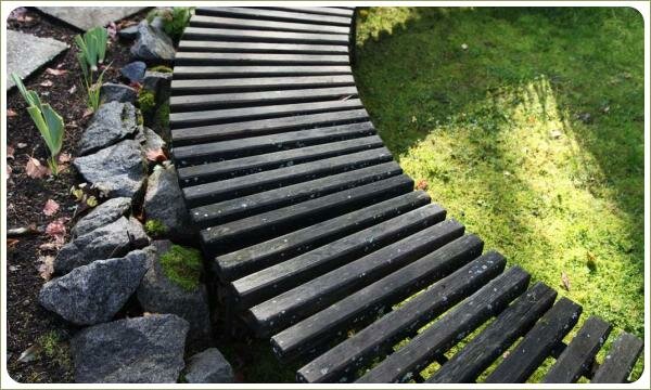 Сиденье из тонких плашек на фоне зелёной лужайки и камней