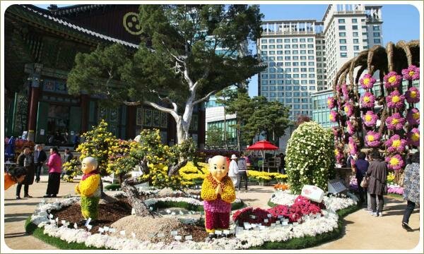 Человеческие фигурки с одеждой из цветов на фоне деревьев увитых цветами и цветущих полян