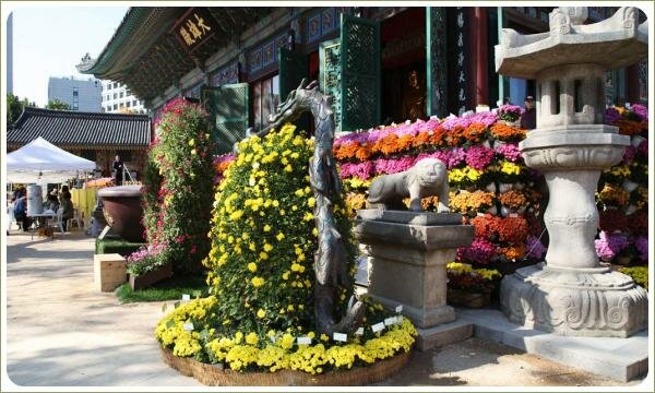 Мифические фигурки и большой буддийский фонарь рядом с каскадными композициями из жёлтых цветов