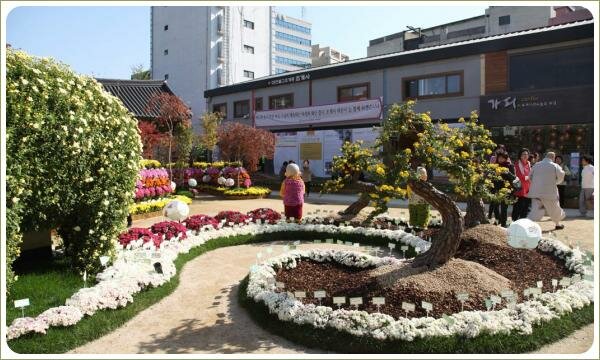 Извилистая лента из цветущих белым растений и подбитая полоской зелёной травы с деревьями усыпанными цветами и фигурками из цветов 