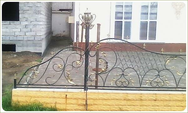 начальный фрагмент ажурного кованого забора на фоне недостроенного здания и здания с финишной отделкой