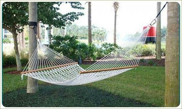 Уютный гамак: на опорах Классический гамак подвязан к толстым стволам деревьев на фоне газона и посадок