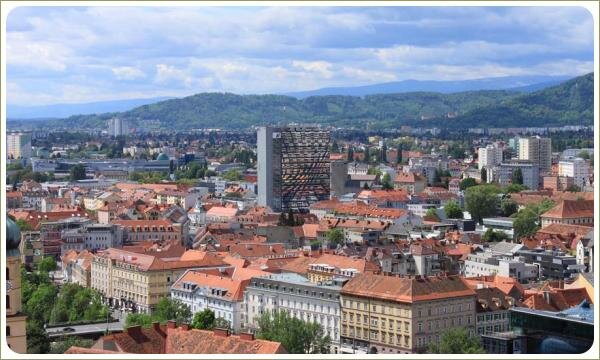 Черепичные крыши многоэтажных домов на фоне горы поросшей деревьями