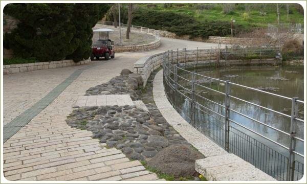 Мощение прямоугольными брусками и округлыми камнями на фоне ограждения берега пруда и дорожек