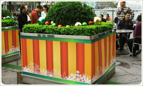 Полосатая тумба на городской площади с зелёными растениями украшенная рождественскими игрушками