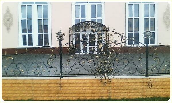 объёмный фрагмент ажурного кованого забора на фоне розового здания