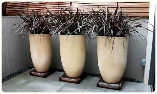 Контейнеры яйцевидной формы с растениями на фоне бамбуковой завесы и мощёной плиткой террасы