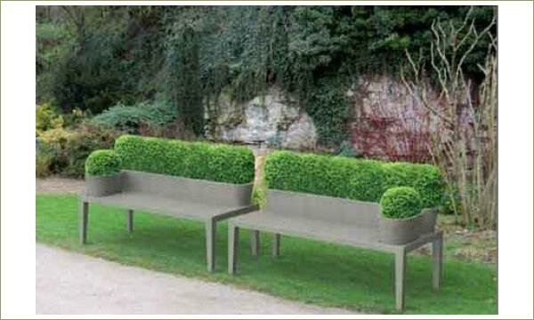Пара скамей со стриженными горшечными кустарниками на фоне скалы и газона