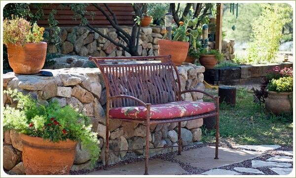 Металлическая кушетка с подушкой на фоне каменной подпорной стенки