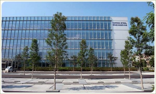 Штамбовые деревья на фоне дорожного покрытия из разноцветных материалов на фоне остеклённого фасада здания