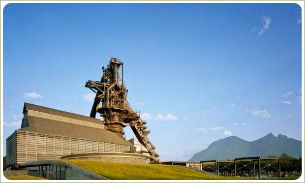 На фоне идустриальных строений из металла покатая крыша со злаками и газон 