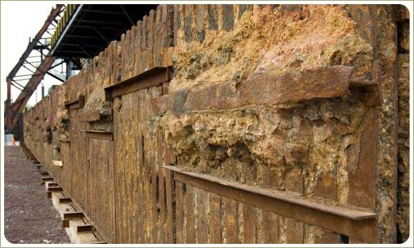 Ржавая конструкция из металла и наполнение породой рыжего цвета выполняет роль забора