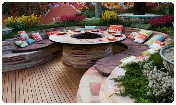 Круглый стол с очагом и скамья из камня вокруг его с яркими подушками