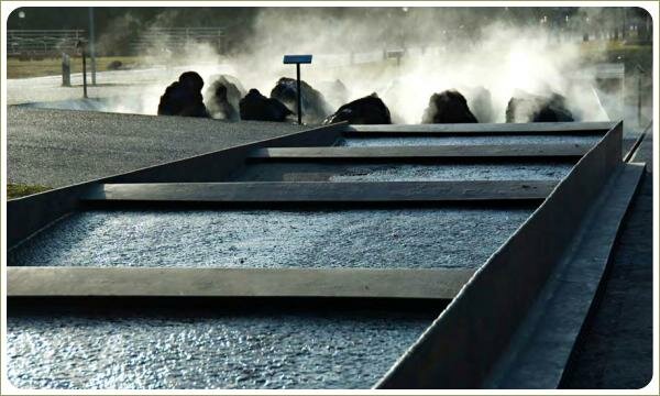 Прямоугольный короб с частыми поперечными перекладинами и водой на фоне крупных камней и пара и дорожек серого цвета