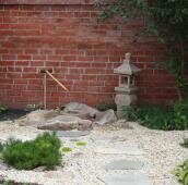 Традиционные японские сооружения ритуального назначения на фоне красной стены из кирпича и белой гравийной отсыпки и растений