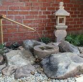 Цукубаи в саду с японским акцентом Культовые японские сооружения на фоне стены из красного кирпича и гравийной отсыпки и растений