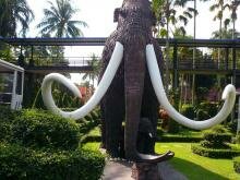 Большая скульптура в виде мамонта с огромными бивнями на фоне тропических растений