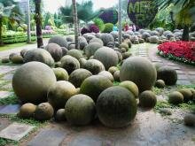 Каменные шары различного расмера на мощёной камнем площадке на фоне ярких тропических композиций