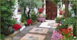 Маленький двор с мощением камнем и яркими растениями в горшках на фоне белых стен строения