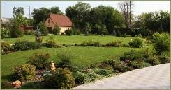 Цветущие кустарники и многолетники вдоль мощёной камнем дорожки на фоне зелёной лужайки