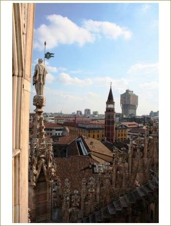 Крыши домов с красной черепицей, статуя святого на вершине одной из башен Собор Дуомо