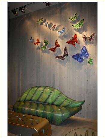 зеленый диван в вид листа,стены из деревянных брусков, бабочки из мозаики на стене