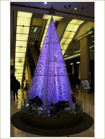 Ажурная ель состоящая из множества снежинок в холле на фоне эскалатора